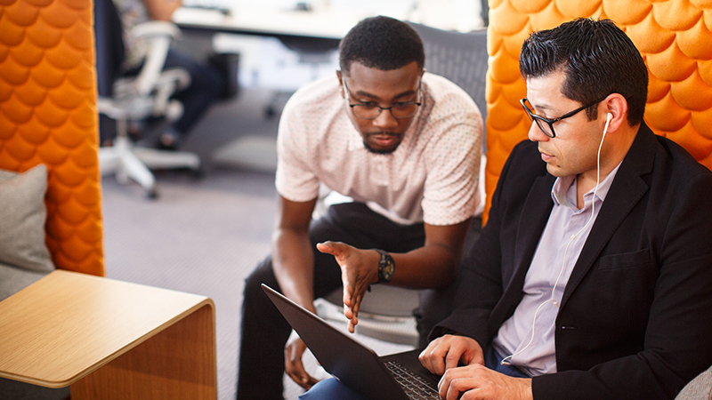 Two seated men discussing laptop display.